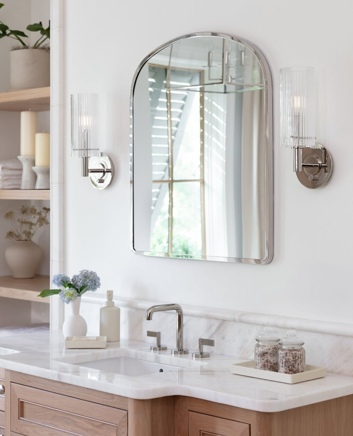 Bathroom vanity with a polished nickel arched mirror, and polished nickel sconces above a sink.