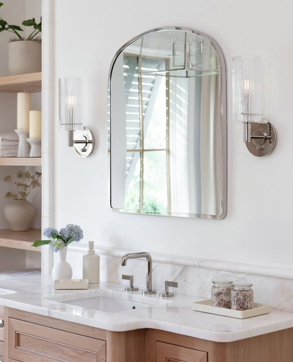 Bathroom vanity with a polished nickel arched mirror, and polished nickel sconces above a sink.
