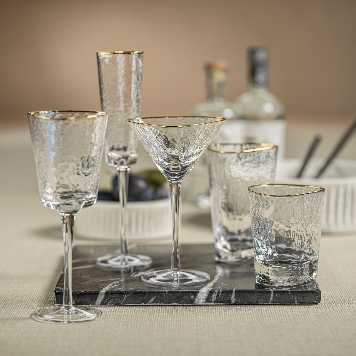 Set of clear glassware with gold rims including wine glasses, martini glasses, and tumblers on a marble tray.