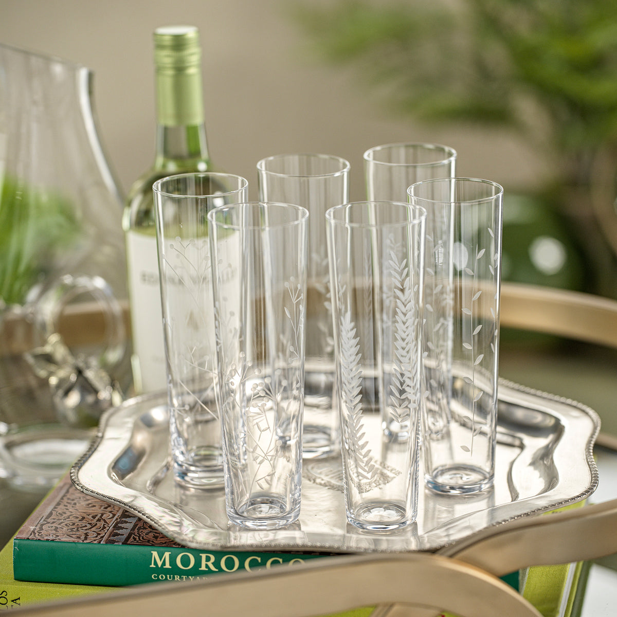 Set of clear glass tumblers on a silver tray with a bottle in the background.