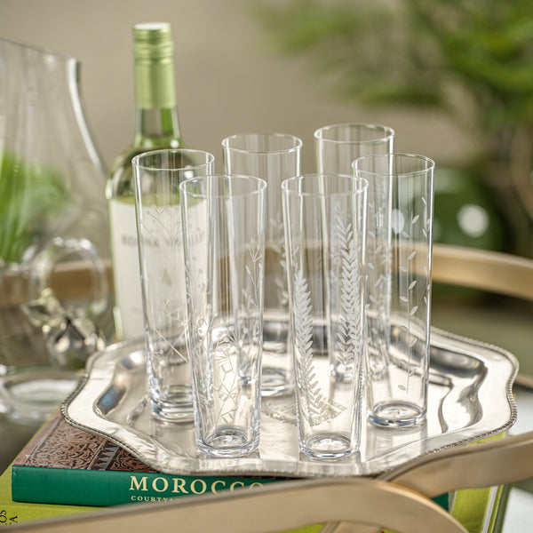 Set of clear glass tumblers on a silver tray with a bottle in the background.