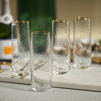 Set of four clear glass tumblers with gold rims on a marble surface.