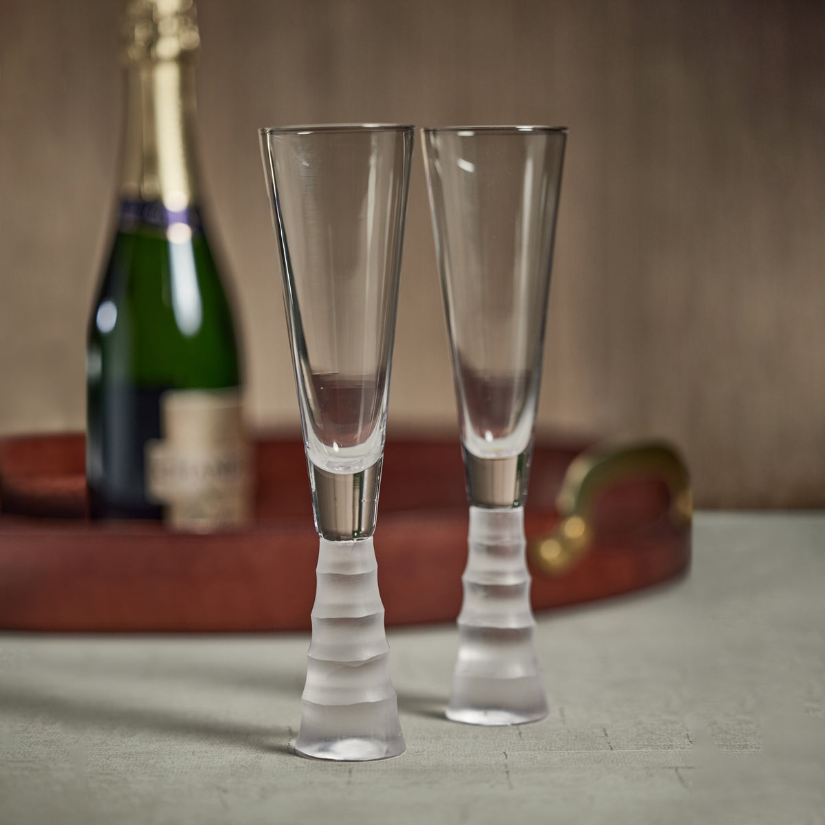 Two clear champagne flutes with a bottle of champagne in the background on a wooden surface.