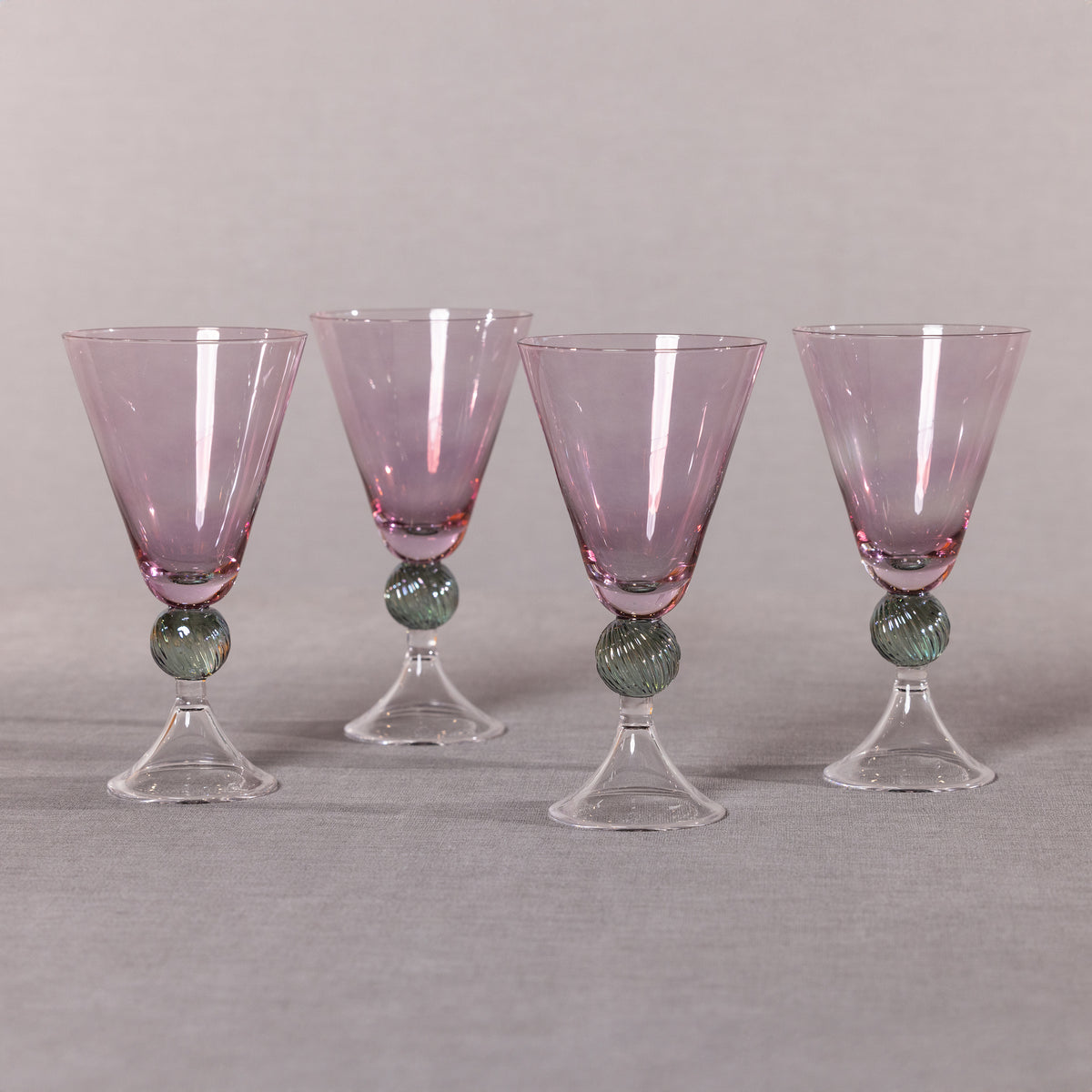 Four purple glass goblets with green marble bases on a gray background