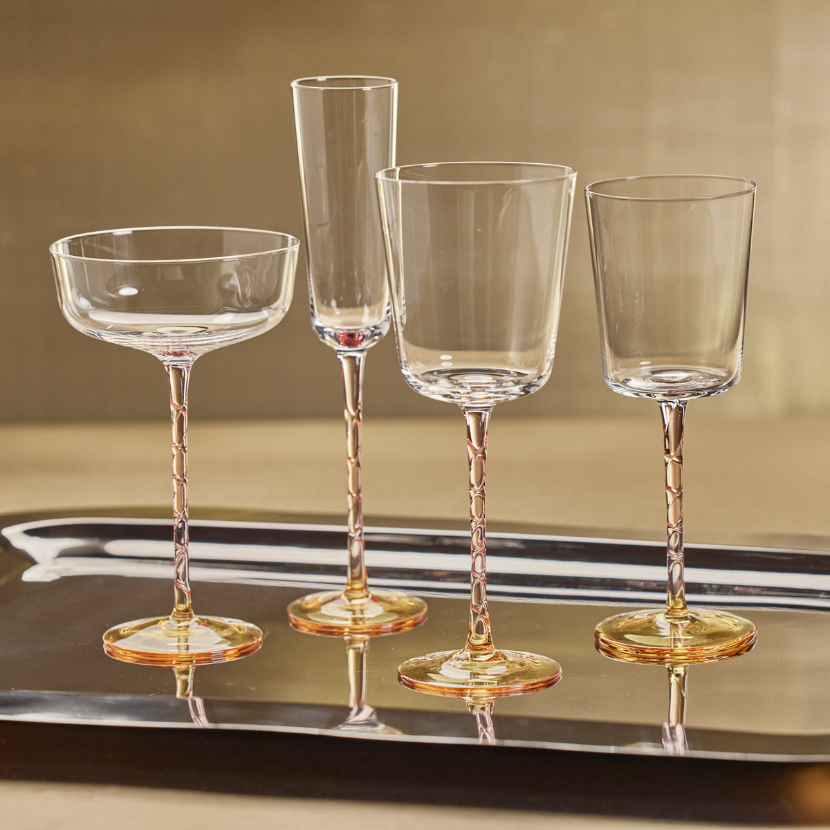Set of four clear glassware on a reflective surface with a gold background