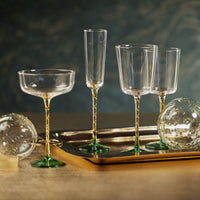 Set of clear glassware with gold and green stems on a dark background