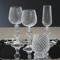 Set of clear glass goblets on a black tray with a dark background