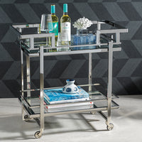 Glass bar cart with bottles, glasses, and books against a geometric patterned wall.