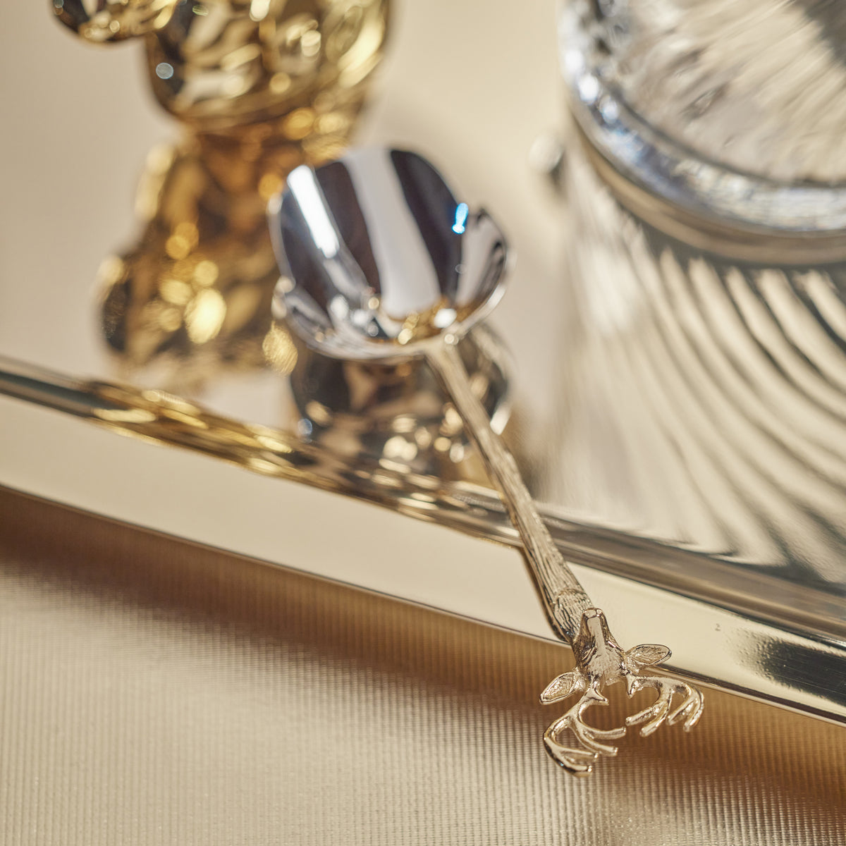 Gold ice scoop with decorative gold stags head handle on a reflective surface