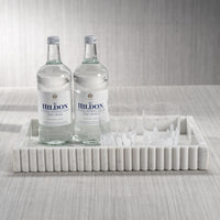 Two bottles of Hildon water on a marble tray with glasses against a neutral background