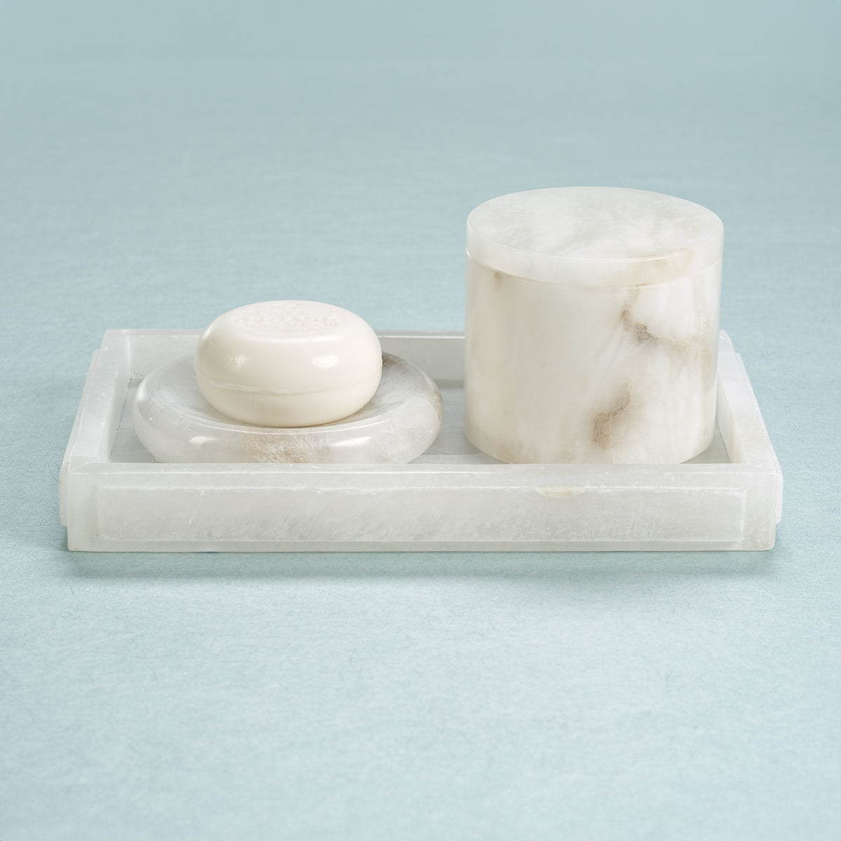 Marble soap dish with a bar of soap and a cylindrical container on a light blue background