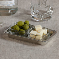 Small glass containers with olives and cheese on a textured surface with a bottle and glass in the background.