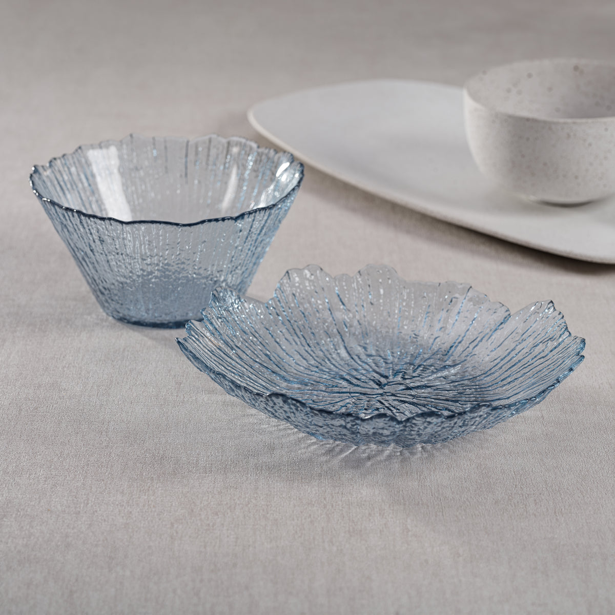 Two blue glass bowls on a gray surface with a white plate in the background.